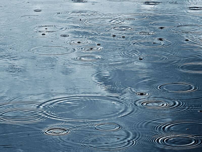 Auf einer Wasseroberfläche sind viele konzentrische Kreise zu sehen, die durch fallende Regentropfen entstehen.
