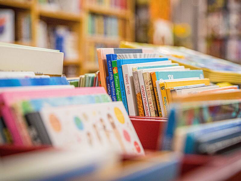 Ein Regal voller bunter Kinderbücher, die in rote Behälter sortiert sind.