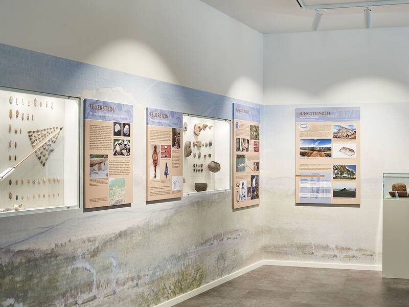 Ein Ausstellungsraum mit Informationstafeln über Feuerstein und die Jungsteinzeit, umgeben von Vitrinen mit archäologischen Fundstücken.