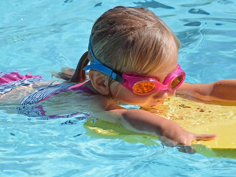 Ein Kind mit pinker Schwimmbrille benutzt ein Schwimmbrett im Pool.