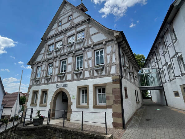 Das Bild zeigt ein traditionelles Fachwerk-Rathaus mit weißen Wänden und braunen Holzbalken, das unter einem blauen Himmel steht.