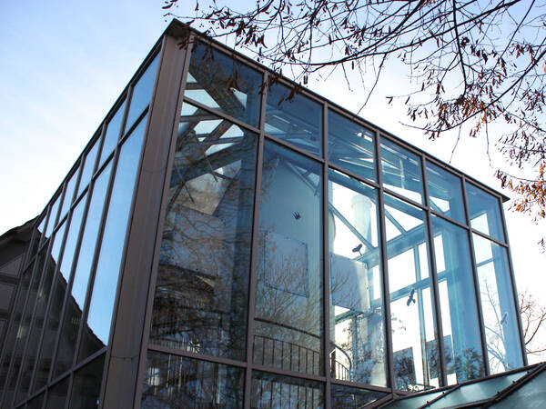 Ein modernes Gebäude mit viel Glas zeigt metallische Strukturen und reflektiert Bäume in den Fenstern.