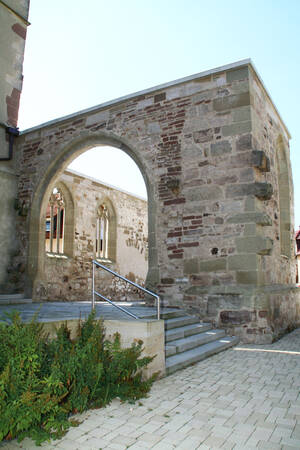 Altes Mauerwerk mit einem großen Rundbogen und einer Treppe, flankiert von Pflanzen.