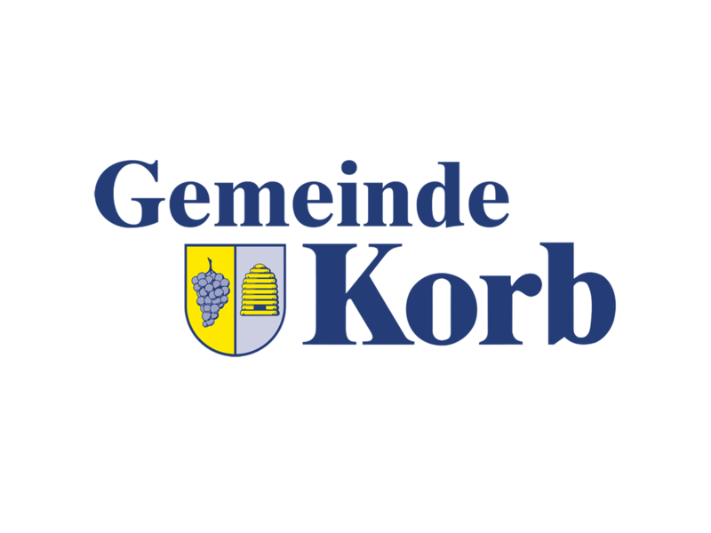 Das Bild zeigt das Logo der "Gemeinde Korb" mit einem Wappen, das eine Traube und einen Bienenkorb auf gelbem Hintergrund darstellt.
