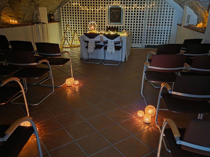 Der Raum ist festlich dekoriert mit Kerzenlichtern und hängenden Sternen, in einem Gewölbe mit Stühlen an den Seiten und einem Tisch im Hintergrund.