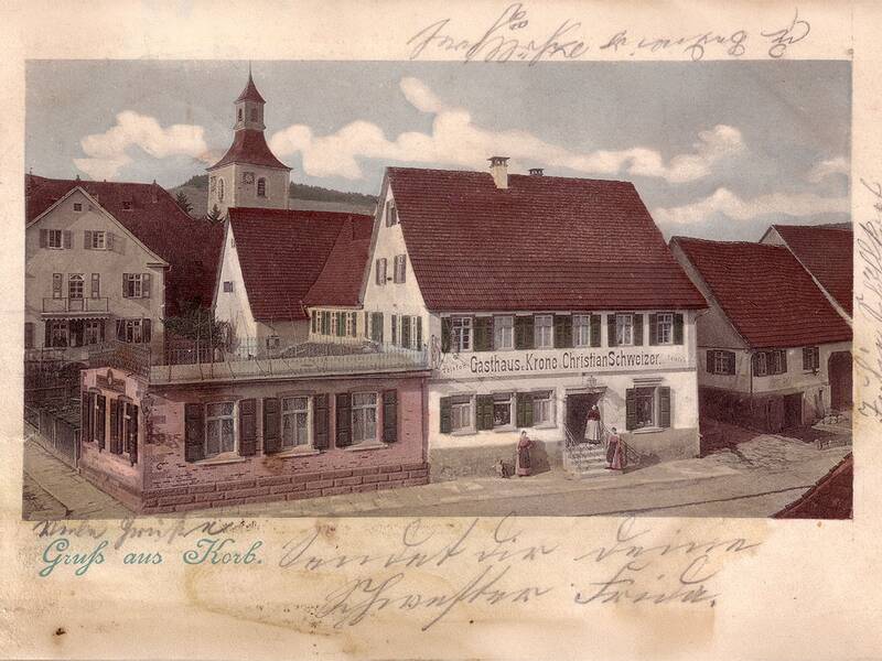 Eine historische Postkarte zeigt ein Dorf mit einem Gasthaus namens "Krone" und angrenzenden Fachwerkhäusern sowie einer Kirche im Hintergrund.